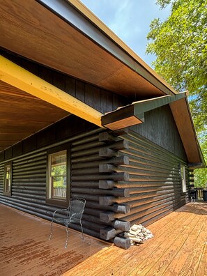 Une cabane en rondins avec une terrasse en bois, une chaise en métal et une pile de bois de chauffage.