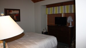 A hotel room with a bed, a lamp, a television, and a dresser.
