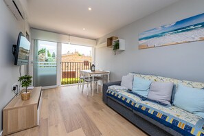 A modern living room with a sofa, a TV, a dining table, and a balcony with a view of the sea.