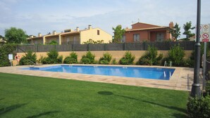 Une piscine rectangulaire, bordée d’une terrasse carrelée, entourée d’une pelouse bien entretenue et d’un petit muret en pierre.