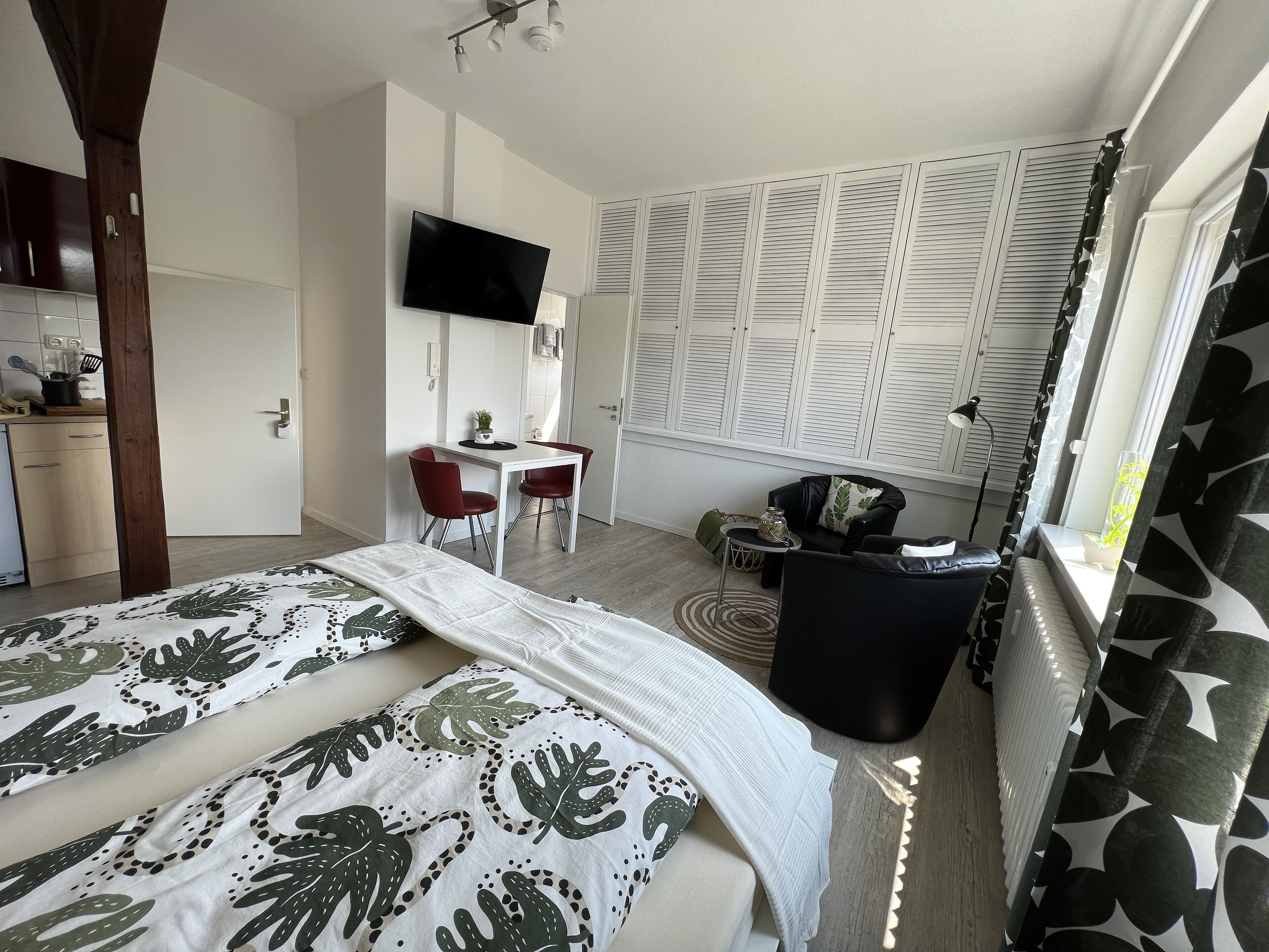 Un dormitorio con cama, escritorio, silla, televisor y ventana con persianas.