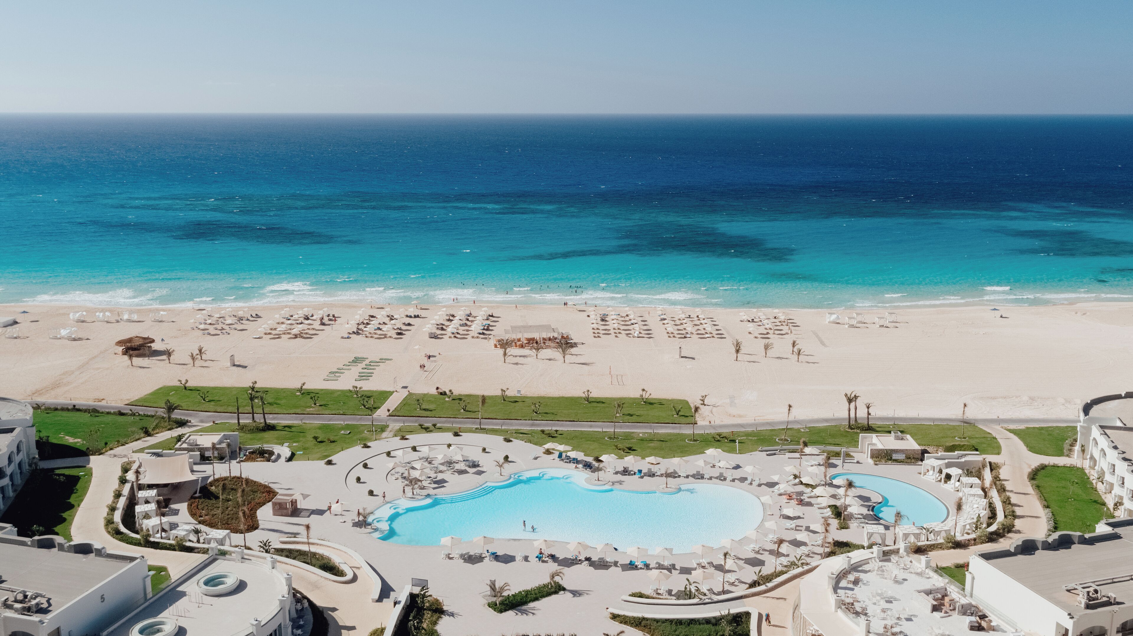 A resort with a large pool, beach area, and ocean view.