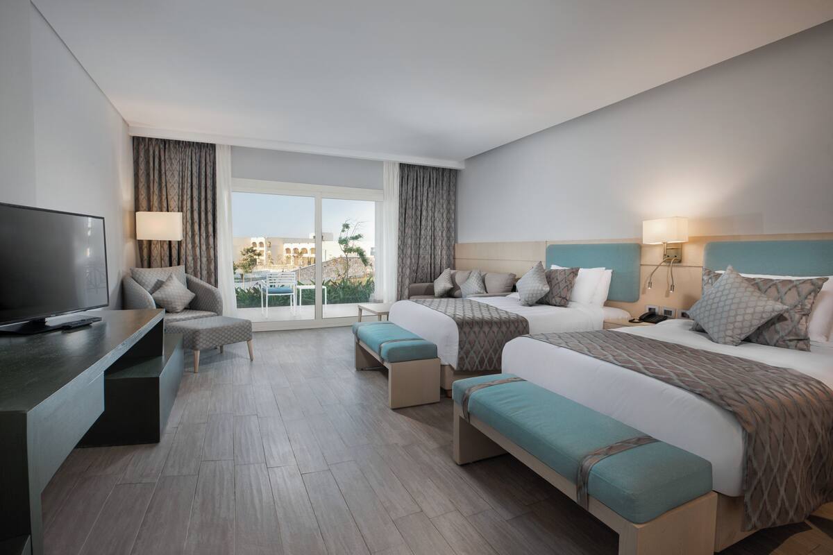 Habitación de hotel con una cama grande, televisión, escritorio y balcón con vistas.