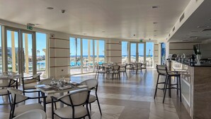 A spacious dining area with large windows offering a view of the pool and ocean. Tables are set with white tablecloths and chairs. - Cleopatra Sidi Heneish (Marsa Matrouh)