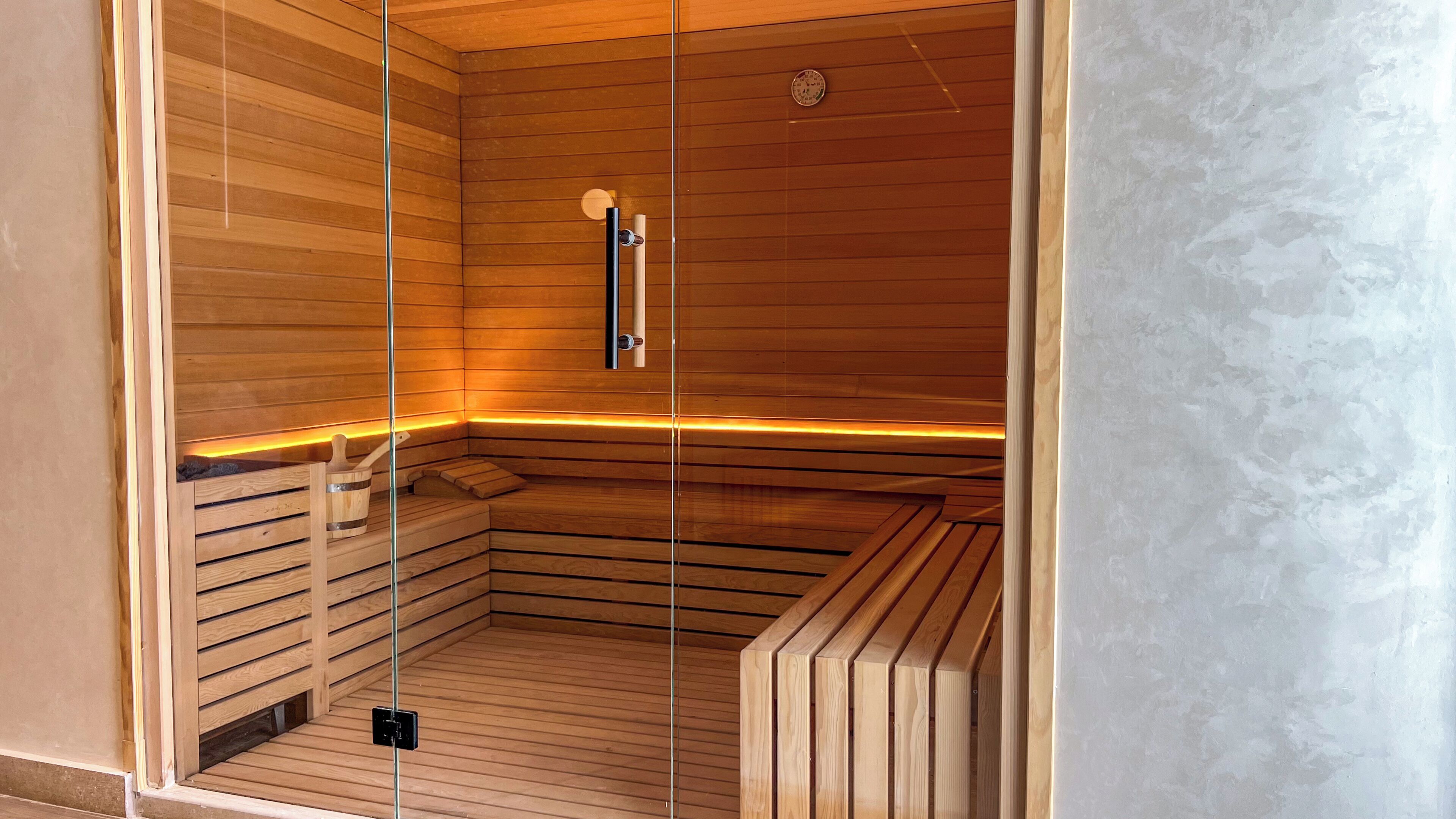 A sauna with wooden walls and benches, a glass door, and a control panel.