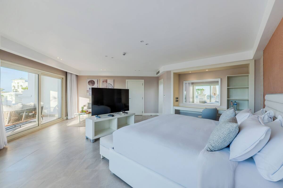 Una habitación de hotel moderna con una cama grande, un televisor de pantalla plana, un escritorio y un balcón con vistas a la ciudad.