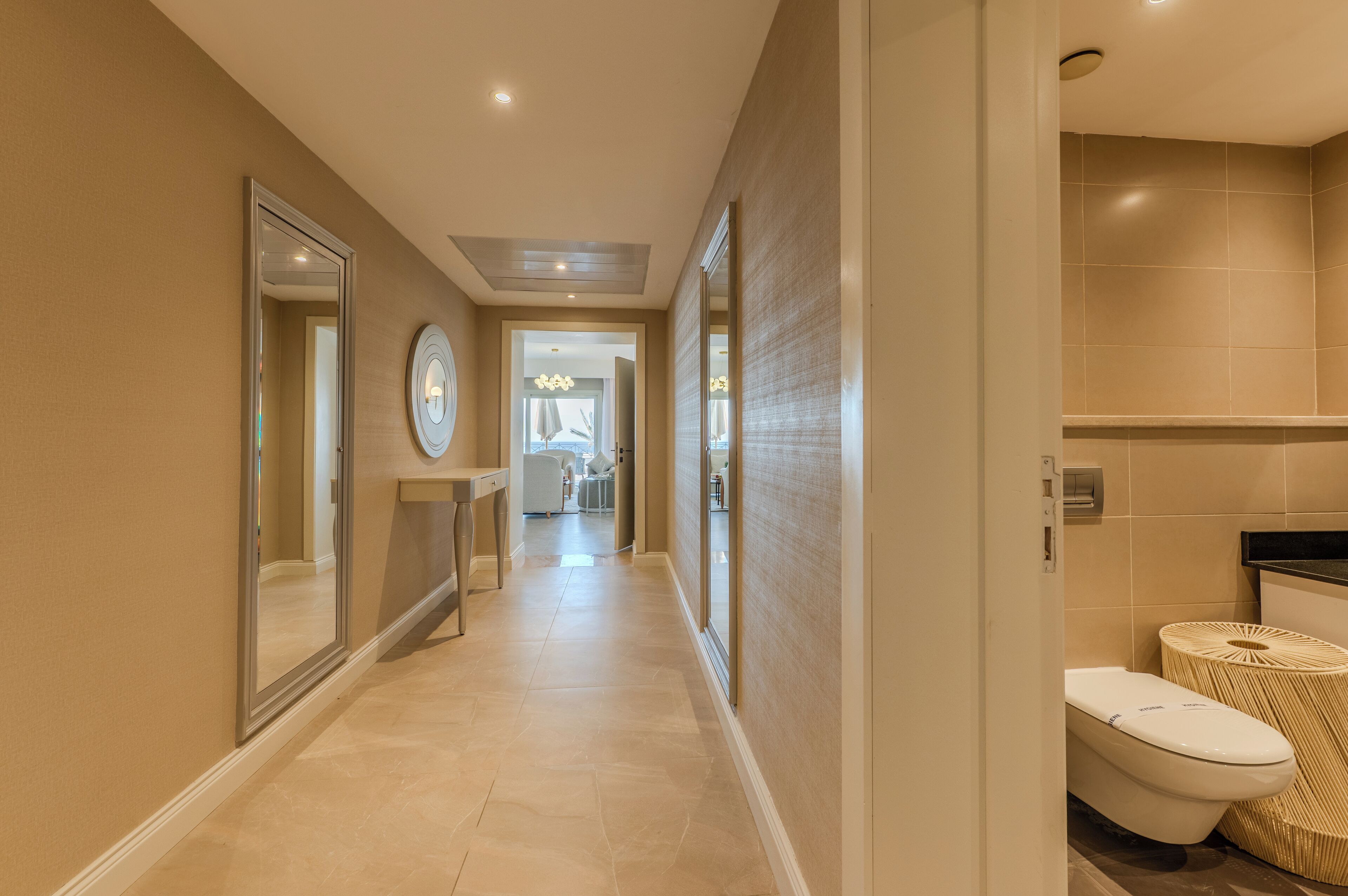 A modern hotel corridor with a bathroom on the right, featuring a toilet, a sink, and a mirror.
