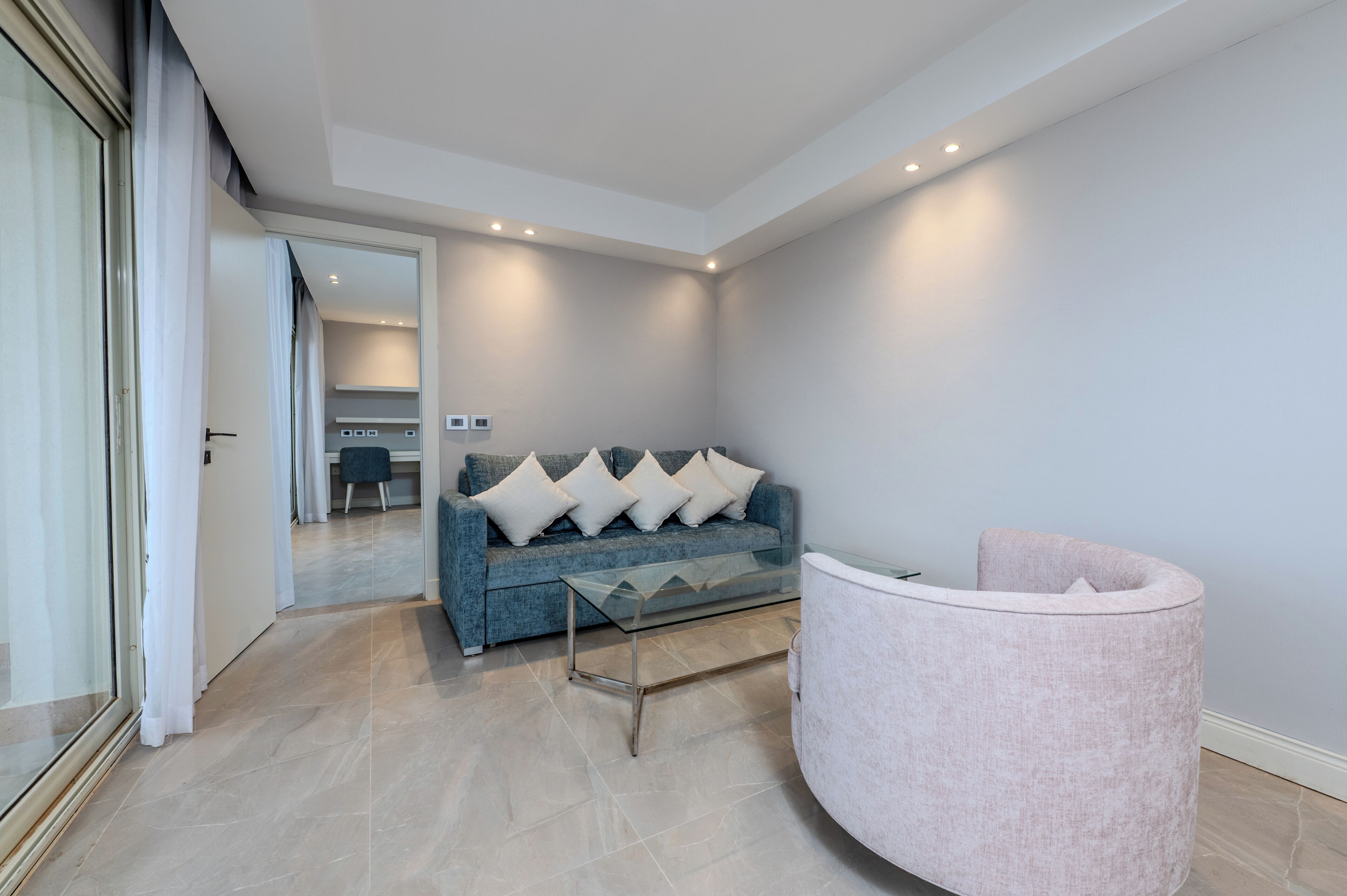 A modern living room with a blue sofa, a glass coffee table, and a pink armchair.