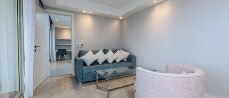 A modern living room with a blue sofa, a glass coffee table, and a pink armchair.