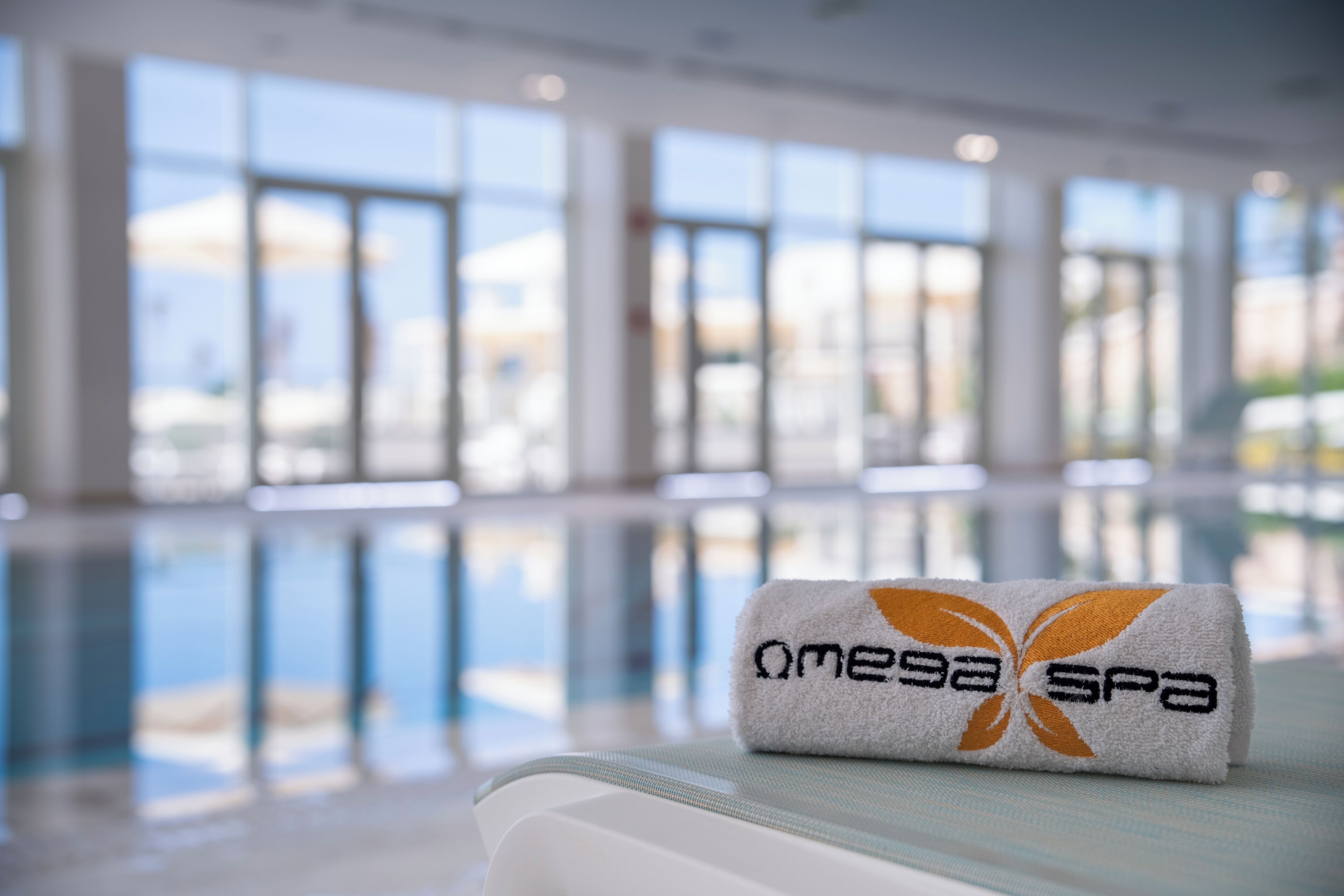Una toalla con la marca 'omegaspa' en una zona junto a la piscina, con amplias ventanas y vistas despejadas a la piscina.