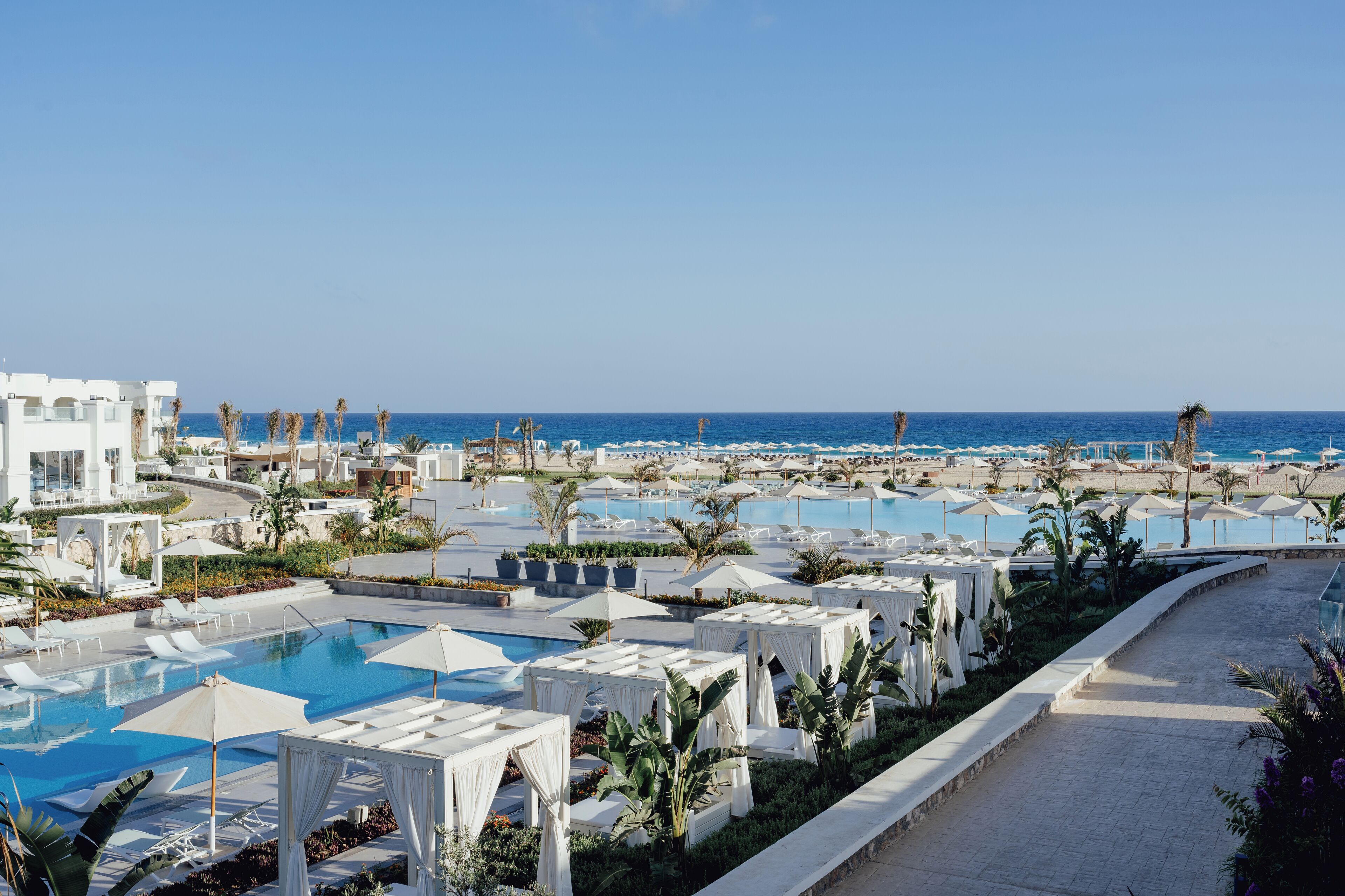 A resort with multiple swimming pools, palm trees, and a clear view of the ocean.