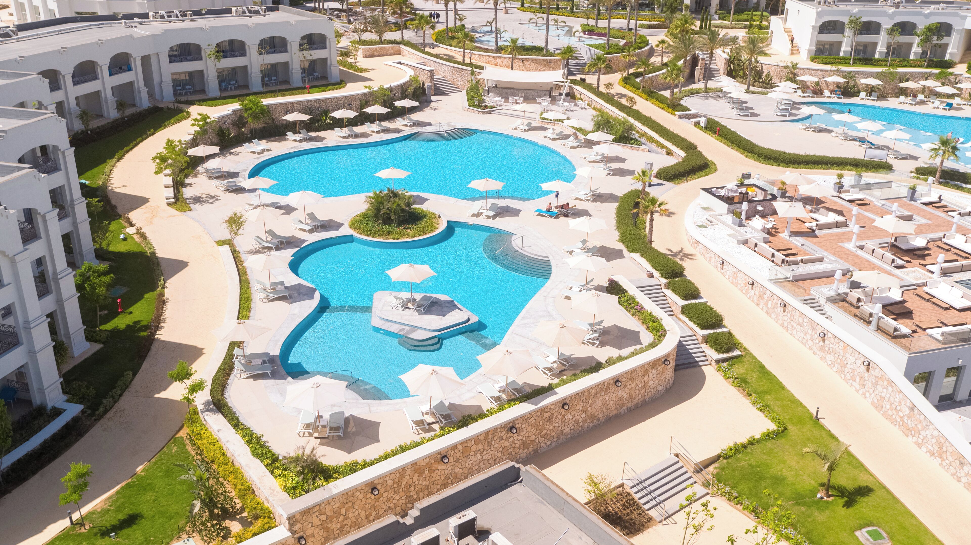 Un resort con varias piscinas, tumbonas y un jardín bien cuidado.