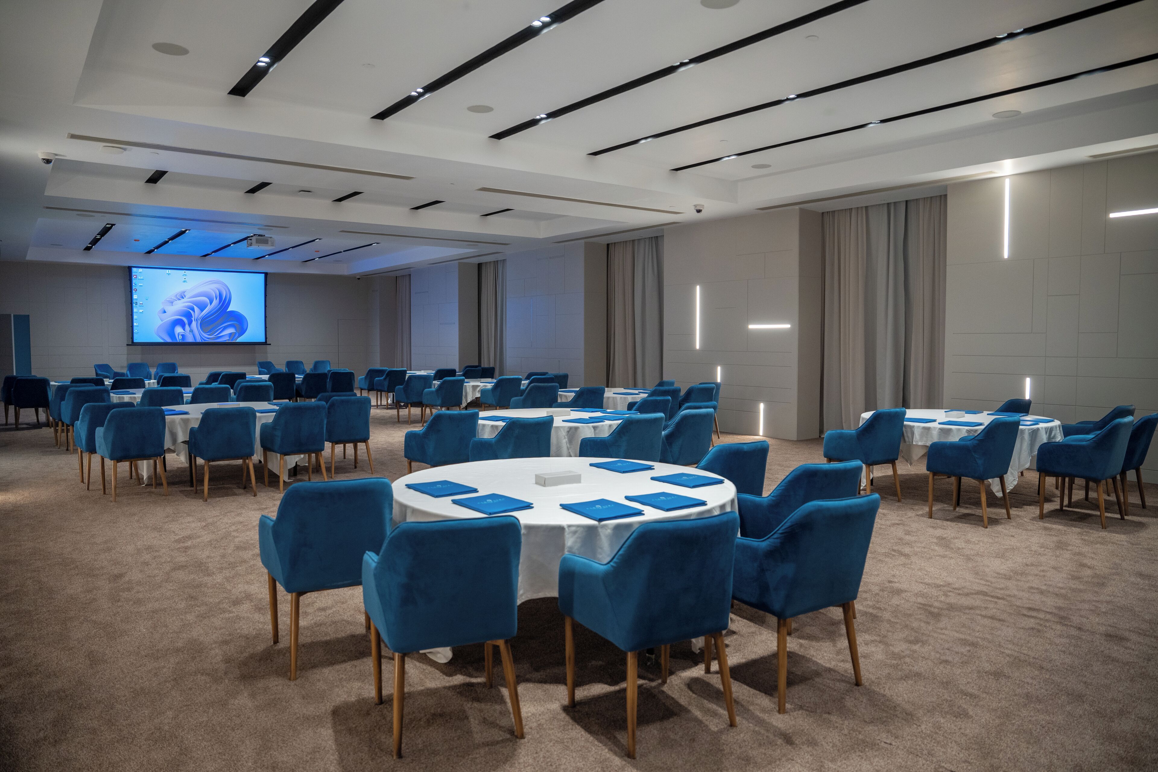 A conference room with round tables, blue chairs, and a large screen for presentations.