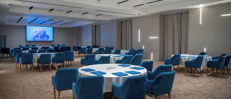 A conference room with round tables, blue chairs, and a large screen for presentations.