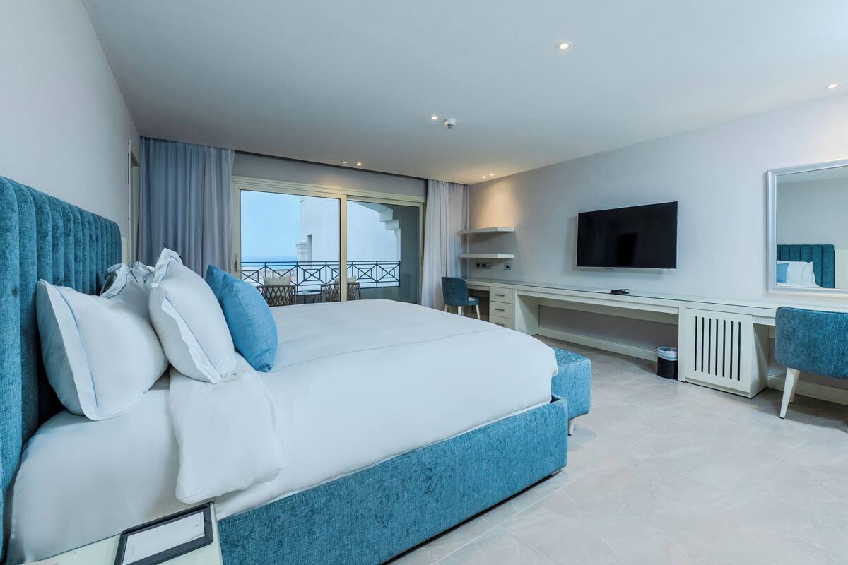 Una habitación de hotel moderna con una cama grande, un escritorio, un televisor y un balcón con vistas al mar.