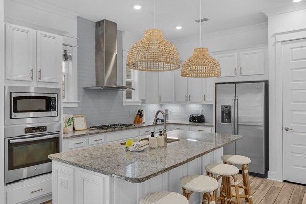 A modern kitchen with white cabinetry, stainless steel appliances, a granite countertop, and wicker pendant lights.