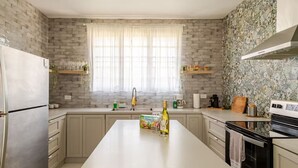 A modern kitchen with a central island, a refrigerator, a stove, and a window with curtains. - 10-minute to the beach from this spacious house for 12 persons (Quebradillas)