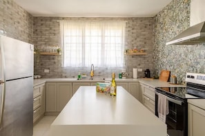 Una cucina moderna con isola centrale, frigorifero, piano cottura e finestra con tende.