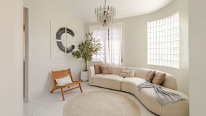A modern living room with a curved sofa, a round rug, a wooden chair, a potted plant, and abstract wall art. - 10-minute to the beach from this spacious house for 12 persons (Quebradillas)