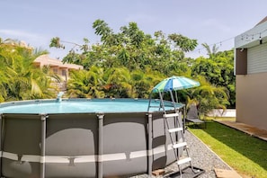 Una piscina con escalera, rodeada de exuberante vegetación y un cielo despejado.