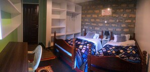 A bedroom with two beds, a desk, and a chair. There is a wardrobe with shelves and a door.