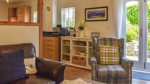 A cozy living room with a brown leather sofa, a plaid armchair, and a dining area with wooden cabinets and a kitchen area. - 2 bedroom accommodation in Cark, near Grange-over-Sands (Cark, near Grange-over-Sands)