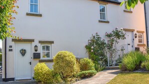 A white cottage with a front door, a small porch, and a garden with various plants and flowers. - 2 bedroom accommodation in Cark, near Grange-over-Sands (Cark, near Grange-over-Sands)