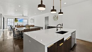 A modern kitchen with a central island, pendant lighting, and a dining area with a view of the outdoors. - Casa Blanca luxury Villa Private pool sleeps 30! (Hurricane)