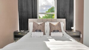 A neatly made bed with pillows labeled "MAKEUP" and a window with curtains.