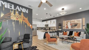 A modern living room with a grey sofa, a black armchair, and a coffee table. There is a kitchen in the background with white cabinets and a microwave.
