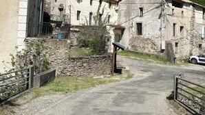 Un pueblo rural con edificios de piedra tradicionales, un camino de grava y un automóvil estacionado al borde de la carretera.