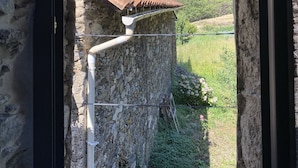 Un edificio de piedra con techo de tejas rojas y una pared de piedra, con vista a un valle verde.