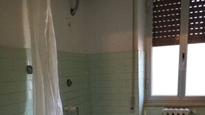 Un baño con bañera, inodoro y ventana con persianas.