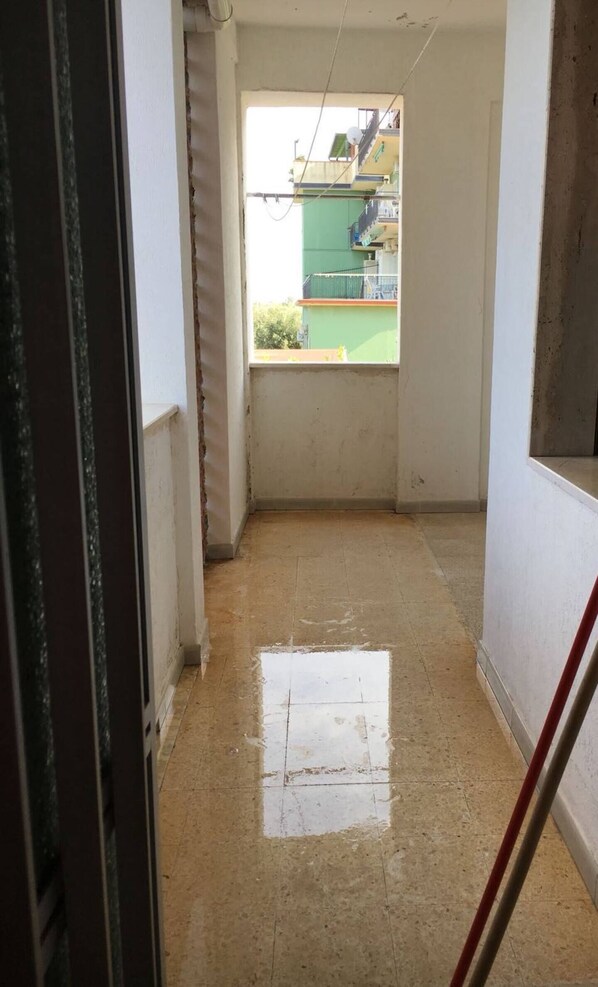 Corredor estreito com chão de azulejos, dando para uma varanda.