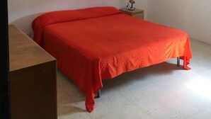 Un dormitorio con una cama individual, una mesita de noche, un ventilador de techo y una pared blanca.
