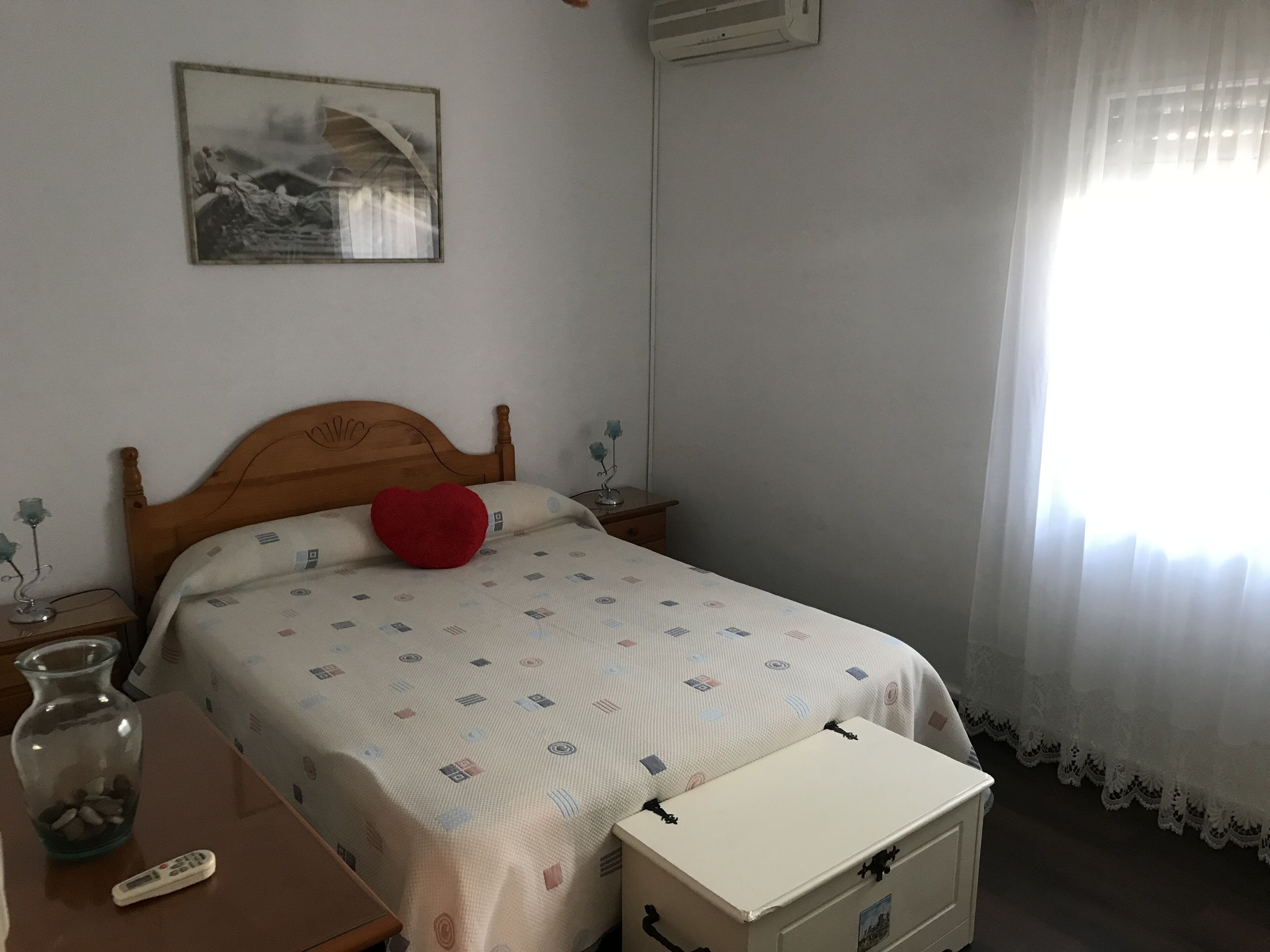 Un dormitorio con una cama de madera, una mesita de noche con un florero, un control remoto y un mueble pequeño.