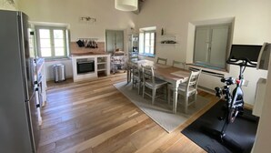 A spacious kitchen with wooden flooring, a dining area with chairs, a built-in oven, and a bicycle in the corner. - The Valley 3 (Castelfalfi)