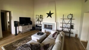 A living room with a sofa, a TV, a fireplace, and shelves with decorative items. - The Valley 3 (Castelfalfi)