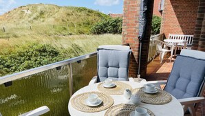 A balcony with a table set for two, two chairs, and a view of a grassy hill. - Düne 77Modern vacation apartment in Westdorf in top location (Baltrum)