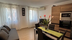 A modern living room with a sofa, dining table with chairs, a vase with flowers, a flat-screen TV, and a built-in oven. - BIENNIAL PENTHOUSE WITH BEAUTIFUL PANORAMIC TERRACE OVER THE LAGOON FREE WI-FI (Venezia)