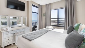 Ein Hotelzimmer mit einem großen Bett, einem Schminktisch mit Spiegeln, einem Flachbildfernseher und einem Balkon mit Aussicht.