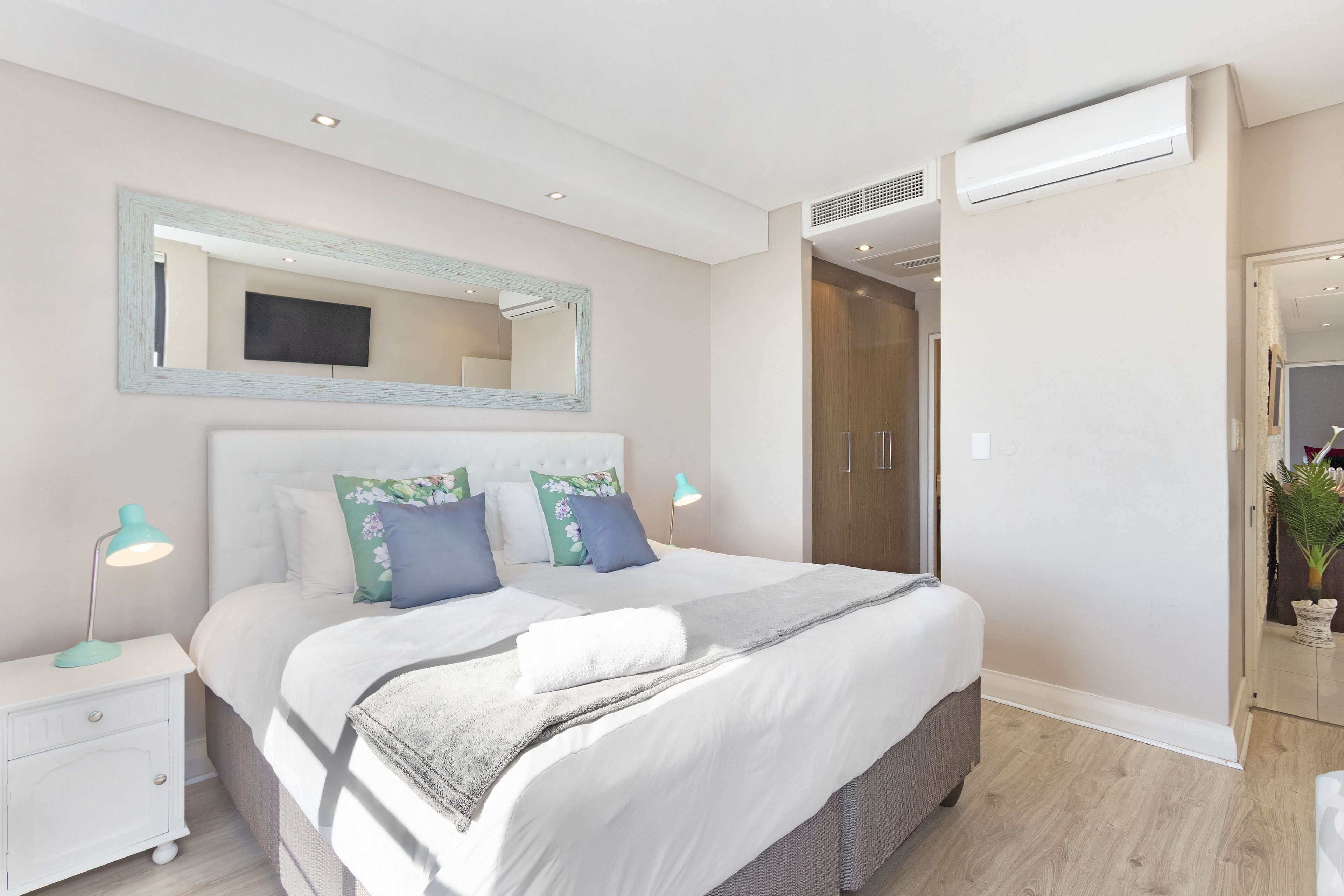 Une chambre moderne avec un grand lit, des tables de chevet, un miroir et un appareil de climatisation.
