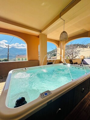 Ein Whirlpool mit Bedienfeld, umgeben von einer Holzdielen-Terrasse und Bögen, mit Blick auf eine Berglandschaft.