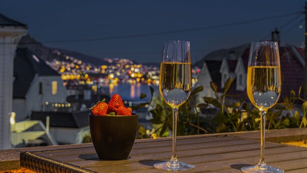 Two wine glasses on a table with a bowl of strawberries in the foreground and a cityscape in the background. - 3 bedroom private vacation home in vestland (Vestland)
