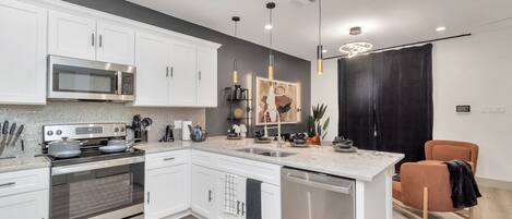 A modern kitchen with white cabinets, stainless steel appliances, a central island, and pendant lighting.