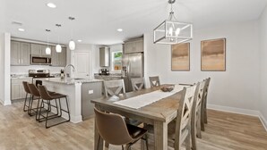 A modern kitchen with a central island, bar stools, and a dining table with chairs. - Beach Vibes in Navarre (Navarre)
