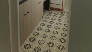 Een badkamer met een witte wastafel, een ronde spiegel met verlichting, een houten trapje en vloertegels met een patroon.