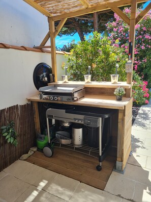 A wooden outdoor kitchen with a built-in grill, a sink, and a small potted plant. - Villa Calme (Sainte-Marie-de-Ré)
