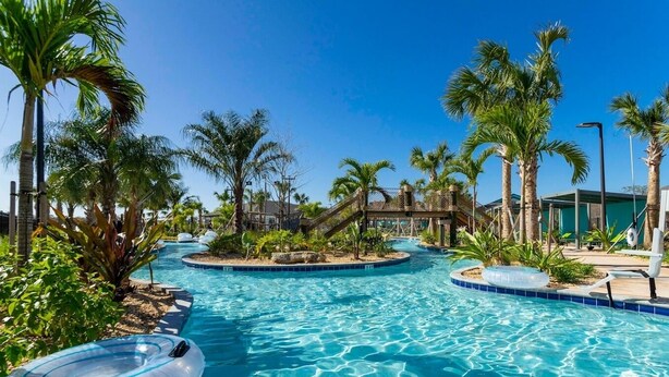 Zona de piscina con múltiples fuentes, palmeras y sillas de descanso.