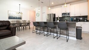 Una cocina moderna con armarios blancos, electrodomésticos de acero inoxidable y una barra con cuatro taburetes.